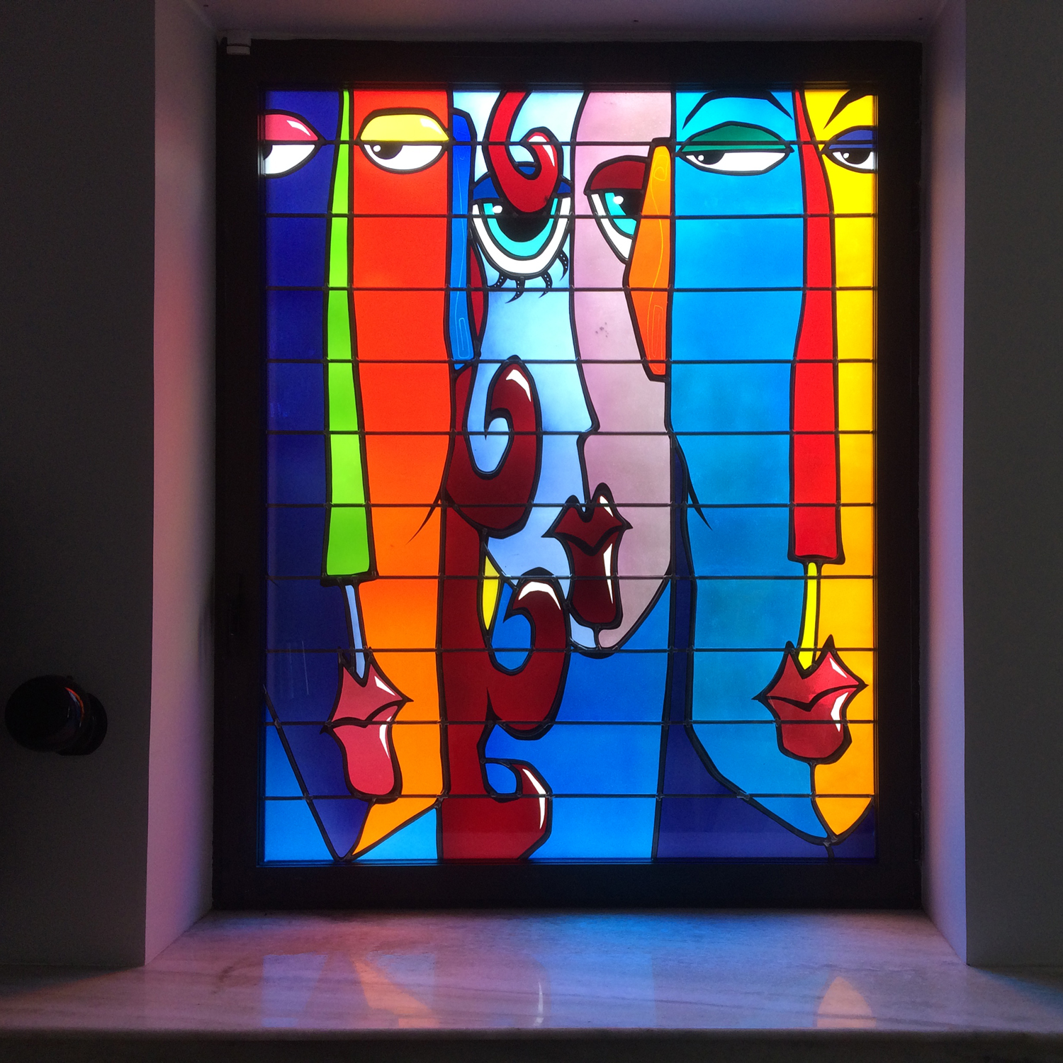 Vitrail contemporain aux visages stylisés et couleurs vives dans une maison